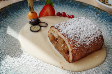 A delectable apple strudel dusted with powdered sugar, served on a sophisticated blue ceramic plate...