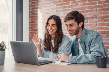 Happy young couple laughing watching funny video or comedy movie online, cheerful man and woman having fun enjoying videocall looking at laptop screen and smiling sitting on sofa at home together.