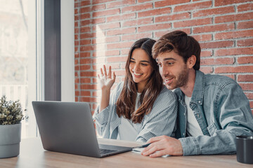 Fototapeta premium Happy young couple laughing watching funny video or comedy movie online, cheerful man and woman having fun enjoying videocall looking at laptop screen and smiling sitting on sofa at home together.