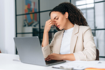 Overworked brazilian or hispanic curly business woman, company employee, working on a laptop in...