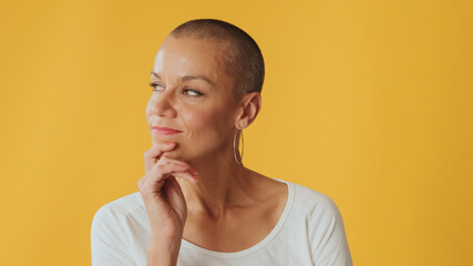 Close-up, pensive young hairless woman, thinking something, having good idea, isolated on yellow background in studio