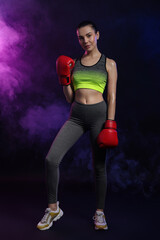 Beautiful woman wearing boxing gloves in color lights and smoke on black background