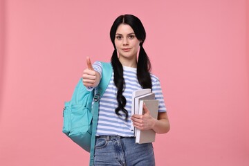 Student with books and backpack showing thumb up on pink background