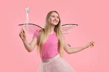 Beautiful girl in fairy costume with wings and magic wand on pink background