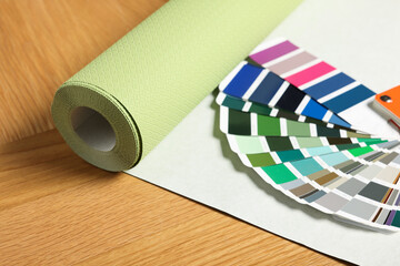 Green wallpaper roll and color palette samples on wooden table