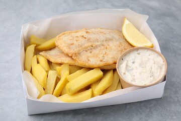 Delicious fish and chips with tasty sauce in paper box on gray table, closeup