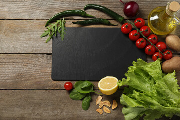 Cooking dinner. Black cutting board and different products on wooden table, flat lay. Space for text