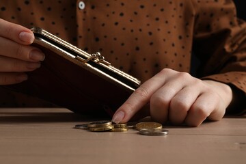 Poverty. Woman with wallet counting coins at wooden table, closeup