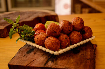 Several fried meatballs, red tomatoes, green lemon cut crosswise and basil branches inside a small...