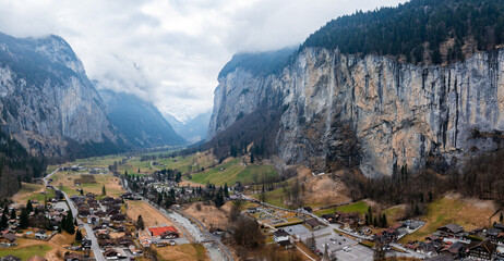 Aerial shot of Murren, Switzerland, shows alpine buildings and a road by a winding river. Cliffs...