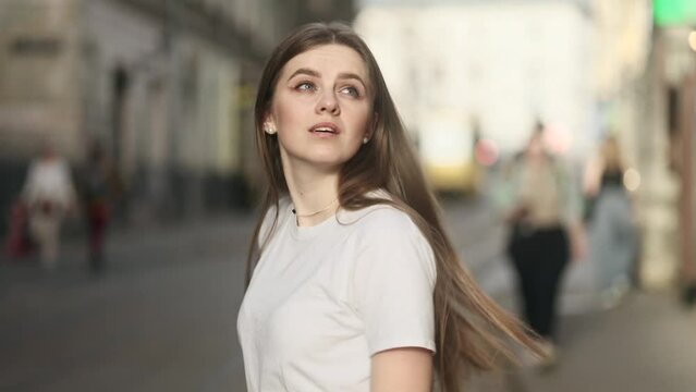 Charming young woman with long hair walking down the street turns around with flying hair outdoors Happy relaxed tourist walking on the city centre enjoying beautiful day alone