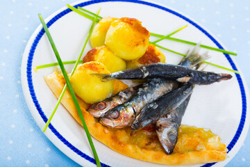 Roasted pilchards served on plate with fried mashed potato balls and focaccia..