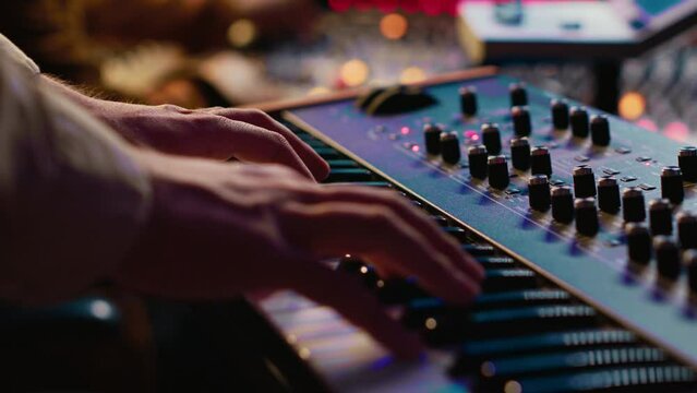 Young singer playing piano electronic keyboard in control room, recording new music with midi controller and mixing console. Talented composer practicing on synthesizer in studio. Camera A.