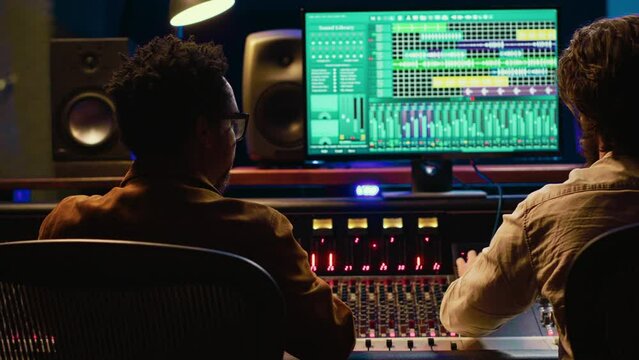 Diverse team collaborating on creating a new hit song in control room, mixing and mastering sounds in post production. Artist and audio expert editing volume level and sound settings. Camera A.