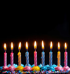 Closeup of the side view of nine lit colorful candles on the top of a birthday cake with copy space