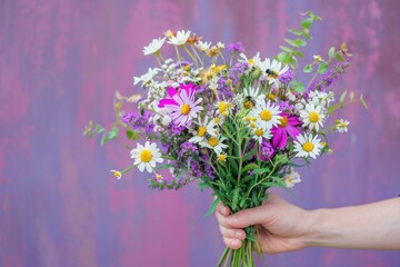 Vibrant summer flower bouquet being delicately held in hand against vibrant purple background, creating a beautiful and colorful contrast