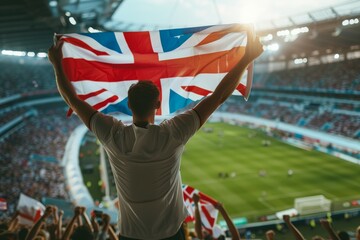 A man is holding a British flag in a stadium full of people. Football fan at the football championship - obrazy, fototapety, plakaty
