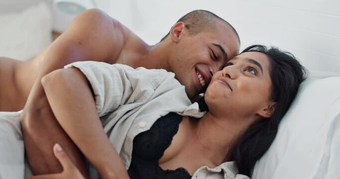 Happy couple, relax and kissing on bed for embrace, love or morning romance in trust or care at home. Young man and woman smile lying in bedroom hug for intimacy, passion or bonding together at house