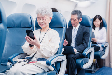 飛行機でスマホを使うシニア女性