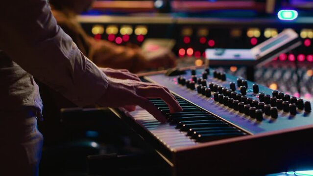 Skilled artist playing piano electronic keyboard in control room, recording new tracks with midi controller and mixing console. Young musician practicing on synthesizer in record studio. Camera A.