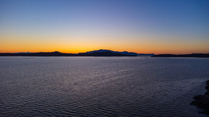 Fototapeta na wymiar Sunset over Thormanby Island. Yellow glow of sun creeping over the low mountains. 