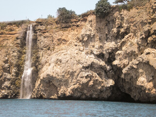 View  from a tourist boat of a waterfall flowing from a mountain into Mediterranean Sea on the coast near the city of Antalya in Turkey