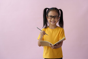 A cute girl wearing glasses holds a pen and writes ideas in a notebook, writes ideas in a planner, and holds a notebook diary. A child with a brilliant idea of time management learning education.