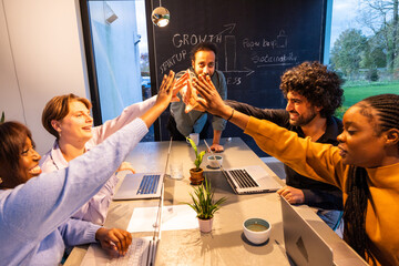 A diverse group of professionals share a high-five in a contemporary office setting, exuding...
