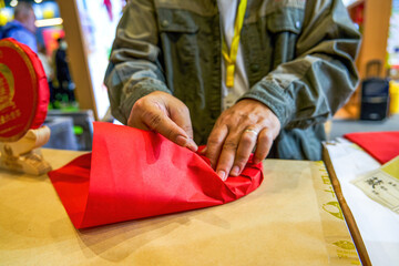 A tea master is wrapping a piece of Pu'er tea cake in red paper