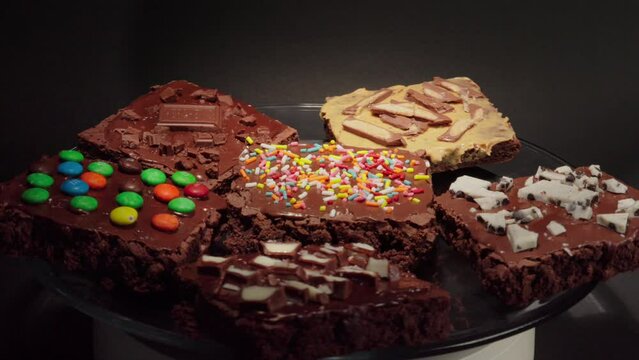 front view Chocolate Brownies plate in turntable spinning in loop with black background mm hershey kinder oreo sprinkles milky way snickers collection