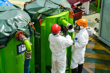 Chemists in protective suits and gas masks work with hazardous materials and toxic wastes, sorting...