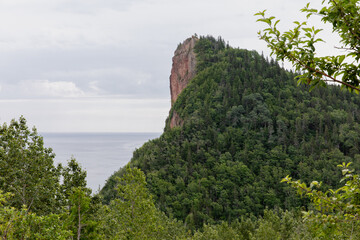 vue sur le sommet d'une montagne en été avec une falaise d'un côté et une forêt de sapin vert de l'autre côté et la mer en arrière plan