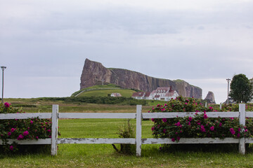 vue sur un terrain avec du gazon vert protégé par une clôture blanche en bois avec une falaise en arrière plan lors d'une journée d'été ennuagée
