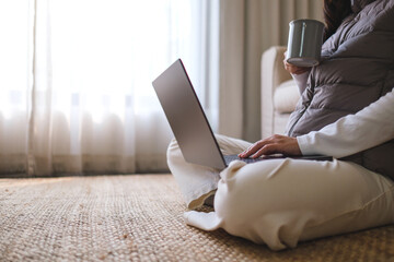 Closeup image of a woman drinking coffee while working on laptop computer at home
