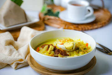 A bowl of “Lontong” or rice cake and coconut gravy with tumeric, chilli, and vegetables with some shadow and selective focus.