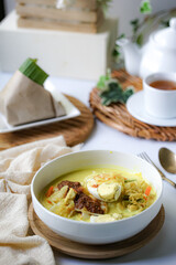 A bowl of “Lontong” or rice cake and coconut gravy with tumeric, chilli, and vegetables with some shadow and selective focus.