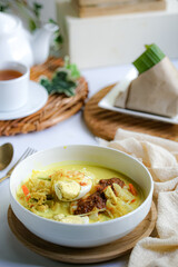 A bowl of “Lontong” or rice cake and coconut gravy with tumeric, chilli, and vegetables with some shadow and selective focus.