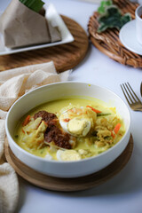A bowl of “Lontong” or rice cake and coconut gravy with tumeric, chilli, and vegetables with some shadow and selective focus.