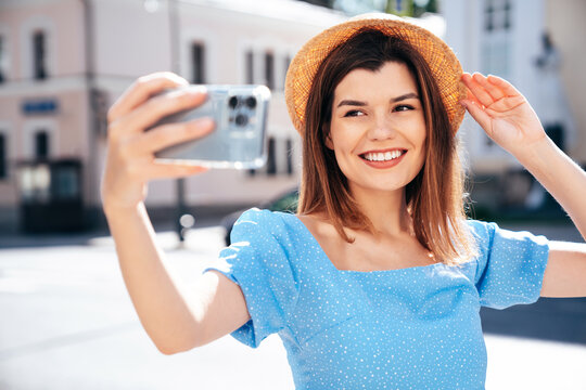 Young beautiful smiling hipster woman in trendy summer blue clothes. Sexy carefree woman posing in the street at sunset. Positive model outdoors. Cheerful and happy and hat. take selfie photos