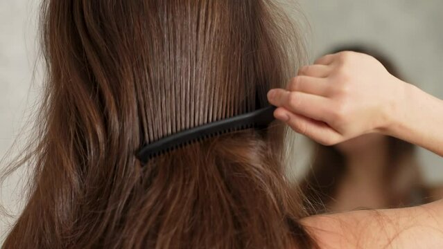 Young woman combing her beautiful hair in front of mirror, rear view