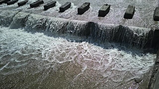chute dentate blocks in concrete water spillway channel slope slowing down the flow of water running down super slow motion captured with a cellphone