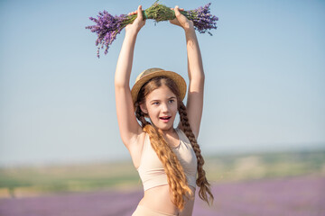 girl is holding a bunch of lavender purple flowers in her hands and wearing a straw hat. She is...