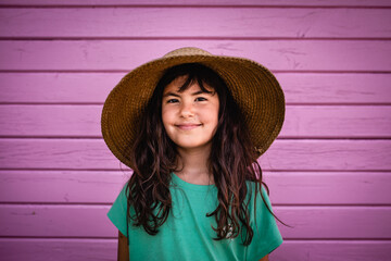 portrait of smiling girl in straw hat against bright pink wall
