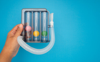 Incentive spirometer. Hand holding a respiratory lung exerciser against a blue background.