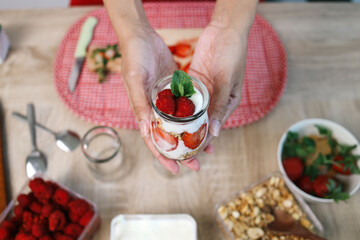 Woman hand holding a glass of strawberry parfait with yogurt and granola