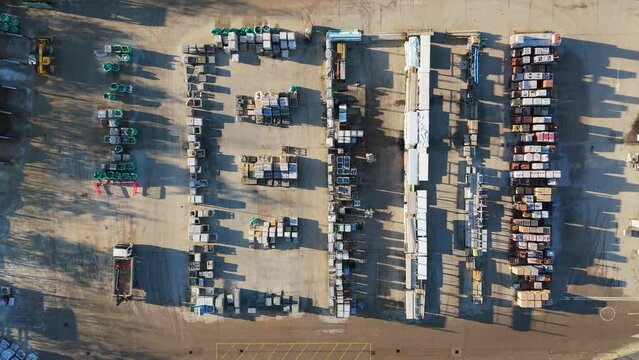Overhead drone aerial footage of industrial, commercial, yard. Storage facility with morning views of workers and vehicle moving around with men at work. Containers and chemical plant machinery