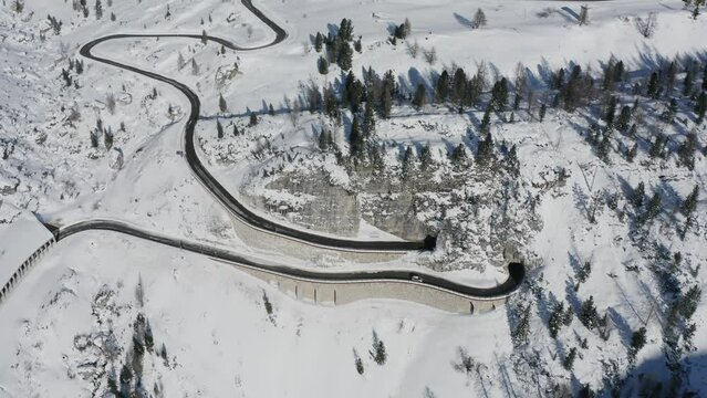 Cars navigate winding Falzarego mountain pass in white Italian Dolomites winter landscape Aerial