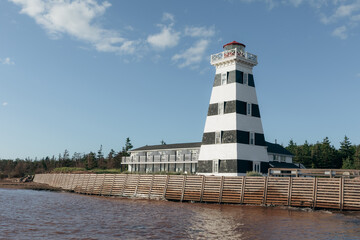 vue sur une auberge avec un phare ligné noir et blanc en bord de mer avec un brise-vague en bois en avant plan