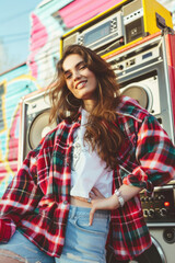 A young woman wearing a vintage flannel shirt and high-waisted jeans, posing in front of a boombox