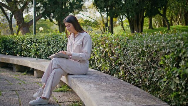 Focused reader studying book in green garden. Serene woman sitting park bench